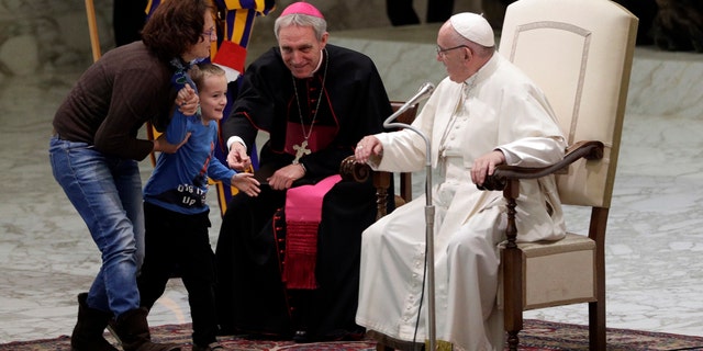 A child is taken away after getting up to the area where Pope Francis is sitting, right, during his weekly general audience in the Paul VI Hall at the Vatican.