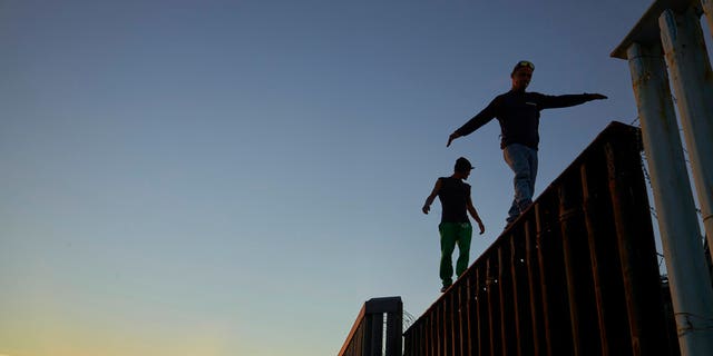 Two Central American migrants walk along the top of the border structure separating Mexico and the United States Wednesday, Nov. 14, 2018, in Tijuana, Mexico. Migrants in a caravan of Central Americans scrambled to reach the U.S. border, catching rides on buses and trucks for hundreds of miles in the last leg of their journey Wednesday as the first sizable groups began arriving in the border city of Tijuana. (AP Photo/Gregory Bull)