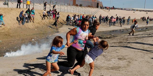 A family of migrants, part of a caravan of thousands of people from Central America heading for the United States, fleeing tear gas at the border wall between the United States and Mexico in Tijuana Sunday.