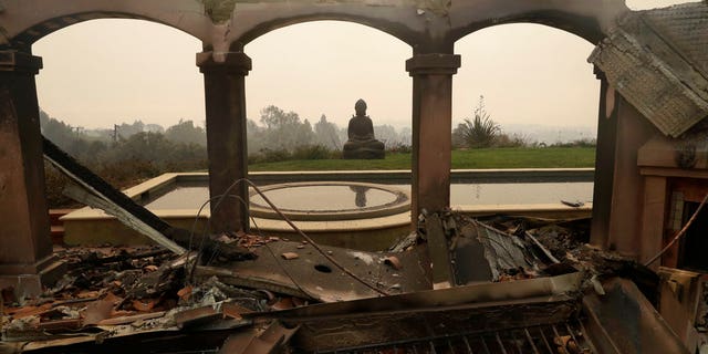 A Buddha statue stands among the damage caused by a wildfire at a home in Malibu, Calif.