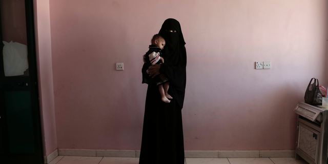 FILE - In this Feb. 13, 2018, file photo, Umm Mizrah, a 25-year-old Yemeni woman, holds her son Mizrah on a scale in Al-Sadaqa Hospital in the southern Yemen city of Aden. The woman, who is nearly into the second trimester of her pregnancy, weighed 38 kilograms (84 pounds), severely underweight. Mizrah, who was 17 months old, weighed 5.8 kilograms (12.8 pounds), around half the normal weight for his age. (AP Photo/Nariman El-Mofty, File)
