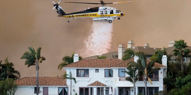 A helicopter drops water on a brush fire behind a home during the Woolsey Fire in Malibu, Calif., Friday, Nov. 9, 2018.