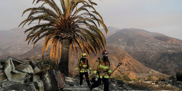 Firefighters Jason Toole, right, and Brent McGill with the Santa Barbara Fire Dept. walk among the ashes of a wildfire-ravaged home after turning off an open gas line on the property Saturday, Nov. 10, 2018, in Malibu, Calif.