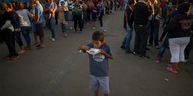 A boy eats as others wait in line for dinner outside of a shelter housing members of the migrant caravan in Tijuana.