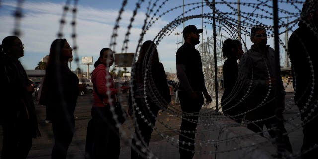 Pedestrians stand near barbed wire at a legal Mexico-U.S. border crossing as they prepare to leave Tijuana, Mexico, Monday, Nov. 19, 2018.
