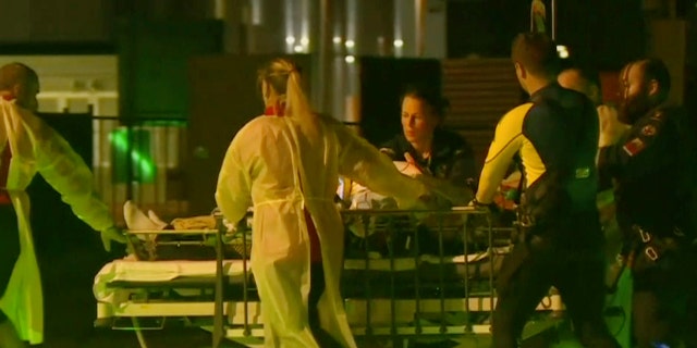 In this Nov. 5, 2018, image made from video, Daniel Christidis, a victim of a shark attack is wheeled on stretcher by paramedics after a rescue helicopter transporting him landed at Mackay Base Hospital helicopter platform in Mackay, Queensland state, Australia.