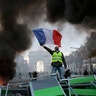 A demonstrator waves the French flag onto a burning barricade on the Champs-Elysees avenue with the Arc de Triomphe in the background, during a demonstration against the rise of the fuel taxes in Paris, Nov. 24, 2018.
