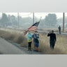 People stand on the side of the road holding an American flag as the motorcade of President Donald Trump drives through areas affected by wildfires in  Chico, California, Nov. 17, 2018. 