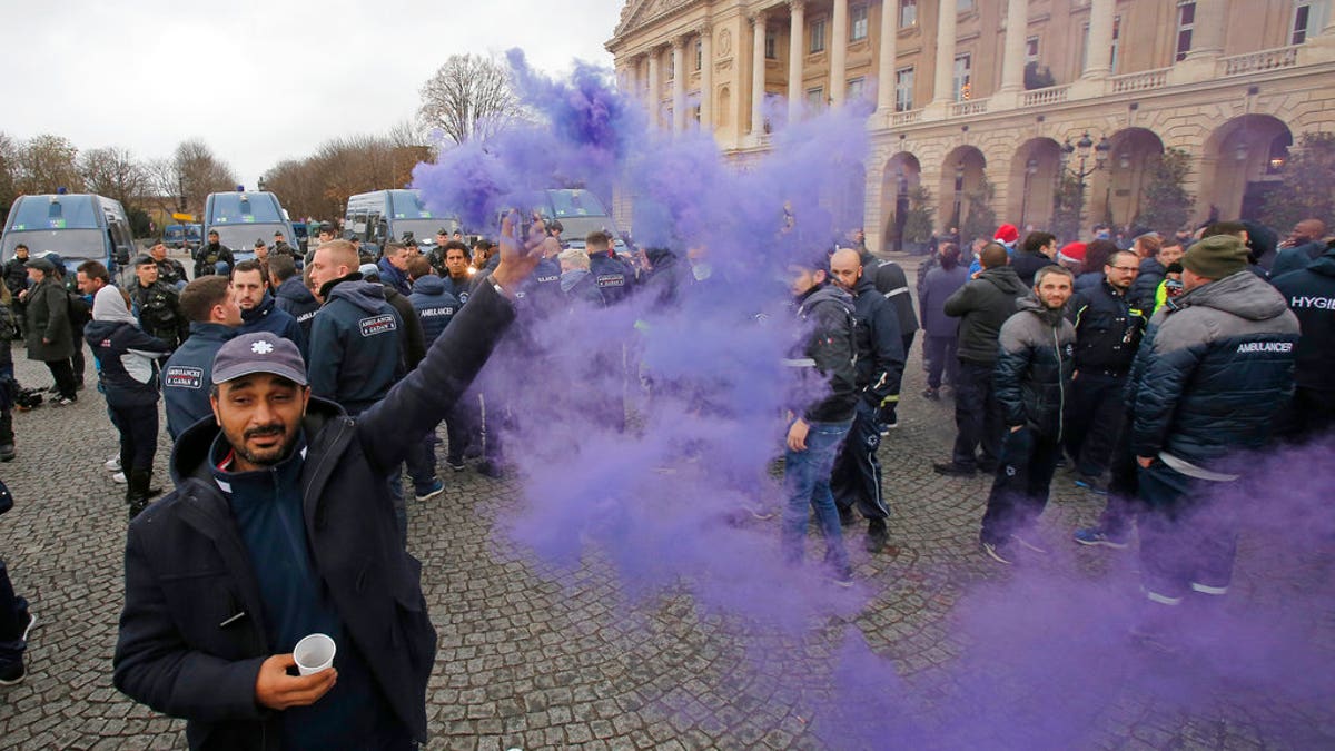 An ambulance worker holds a flare as he and his fellows block the Place de la Concorde in Paris, Monday, Dec. 3, 2018. Ambulance workers took to the streets and gathered close to the National Assembly in downtown Paris to complain about changes to working conditions as French Prime Minister Edouard Philippe is holding crisis talks with representatives of major political parties in the wake of violent anti-government protests that have rocked Paris. (AP Photo/Michel Euler)