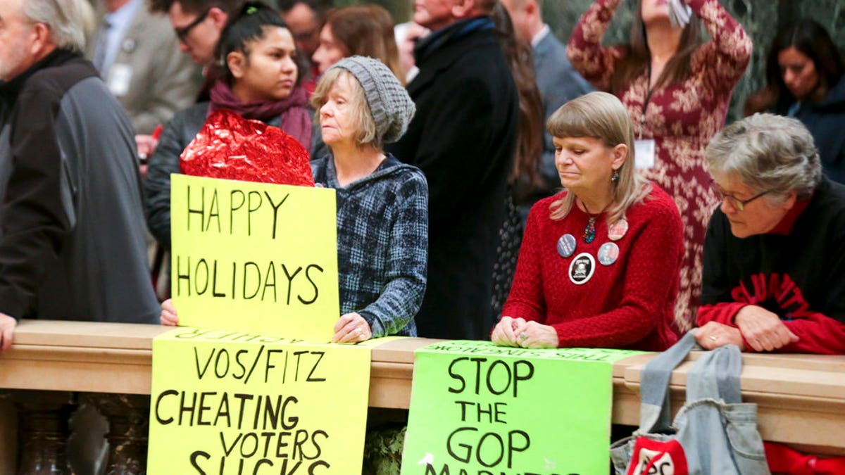 Protesters Peppi Elder, left, and Christine Taylor holds up signs during the state Christmas Tree lighting ceremony in state Capitol Rotunda Tuesday Dec. 4, 2018, in Madison, Wis. The Senate and Assembly are set to send dozens of changes in state law to Gov. Scott Walker's desk. (Steve Apps/Wisconsin State Journal via AP)