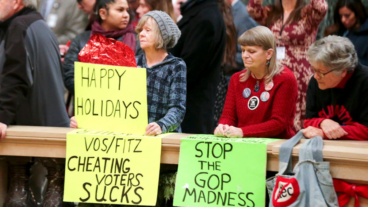 Protesters Peppi Elder, left, and Christine Taylor holds up signs during the state Christmas Tree lighting ceremony in state Capitol Rotunda Tuesday Dec. 4, 2018, in Madison, Wis. The Senate and Assembly are set to send dozens of changes in state law to Gov. Scott Walker's desk. (Steve Apps/Wisconsin State Journal via AP)