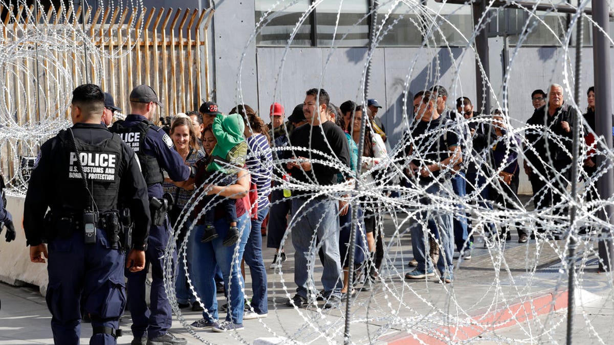 FILE: People line up to cross into the United States from Tijuana, Mexico, seen through barriers topped with concertina wire at the San Ysidro port of entry in San Diego.