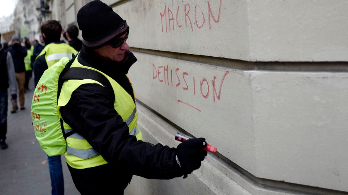 A demonstrator wearing a yellow vest writes a slogan 'Macron resign' on a wall during a protest Saturday, Dec. 15, 2018 in Paris. (AP Photo/Kamil Zihnioglu)