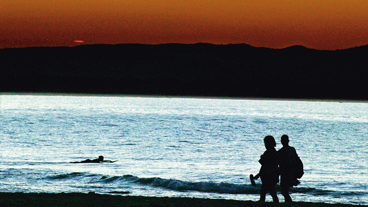 A couple stroll along a Byron Bay beach at sunset.