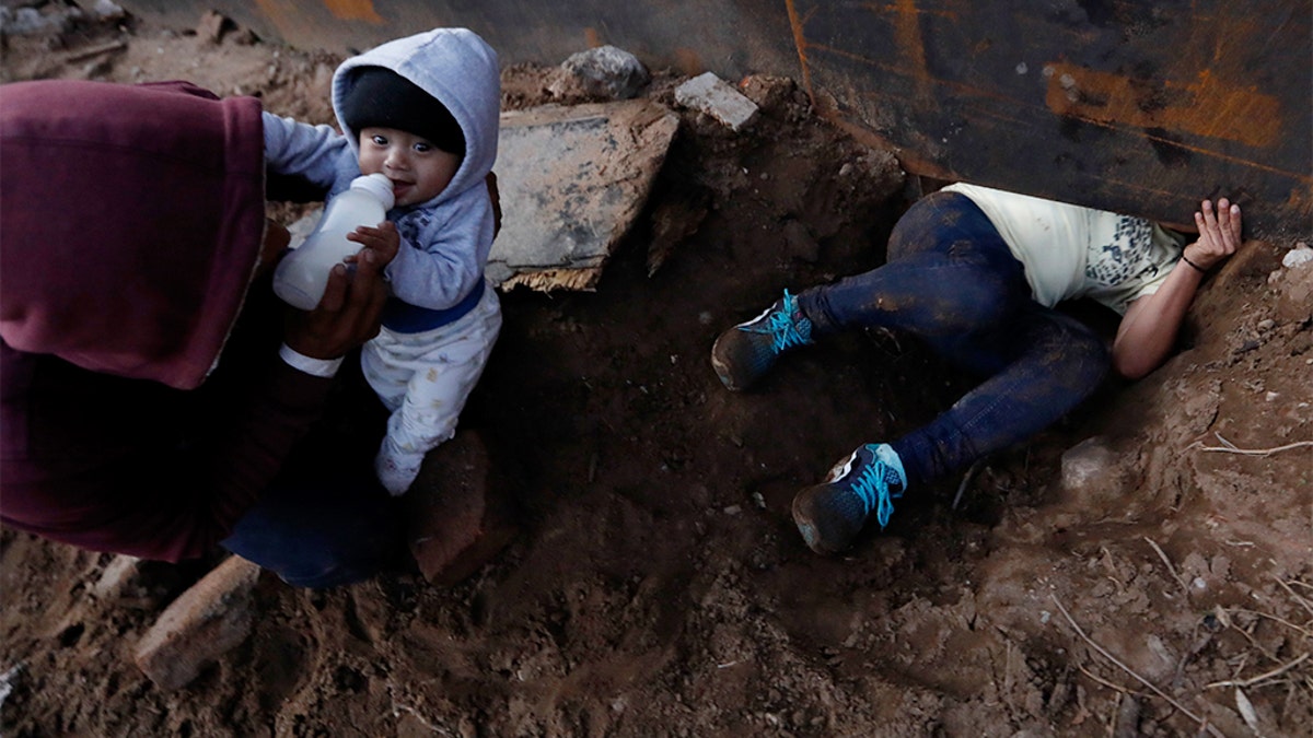 Honduran migrant Joel Mendez, 22, feeding his eight-month-old son Daniel as his partner Yesenia Martinez, 24, crawled through the hole under the U.S. border wall. (AP Photo/Rebecca Blackwell)