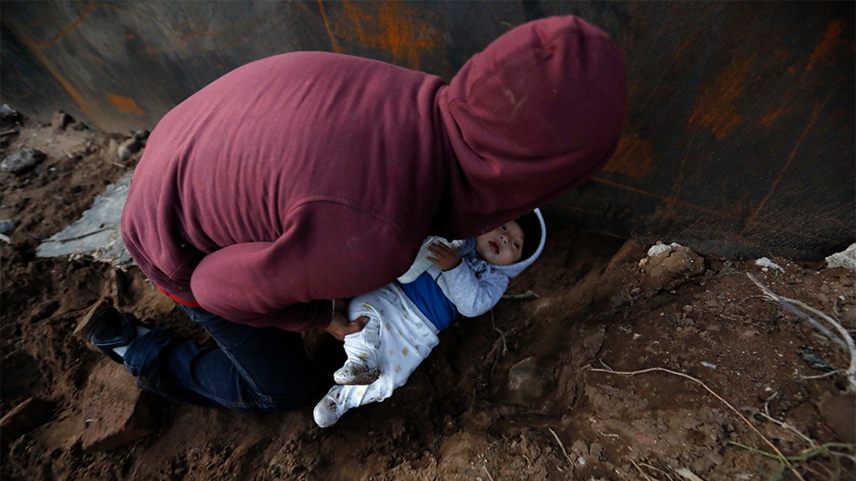 Honduran migrant Joel Mendez, 22, passing his eight-month-old son Daniel through a hole under the U.S. border wall to his partner, Yesenia Martinez, 24, who had already crossed in Tijuana, Mexico, on Friday. (AP Photo/Rebecca Blackwell)