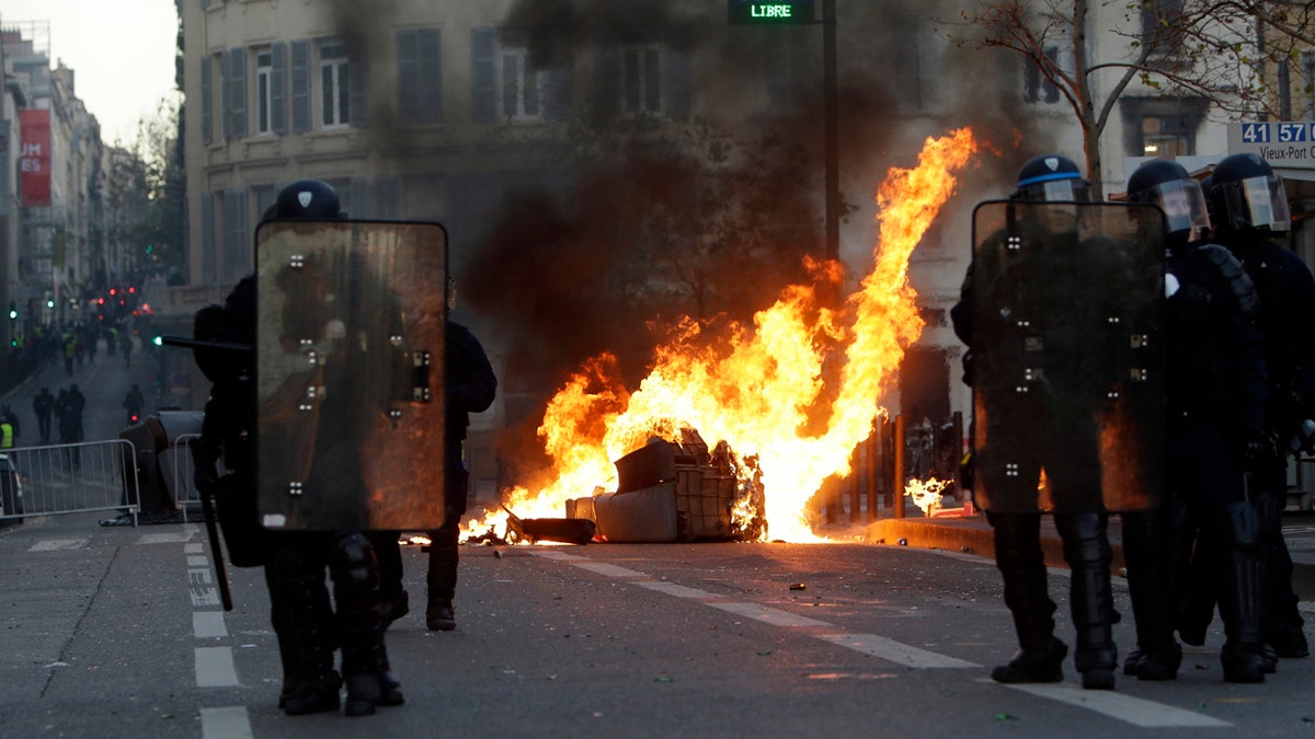 Riot police officer stand in front a burning trash bin during clashes, Saturday, Dec. 8, 2018 in Marseille, southern France.