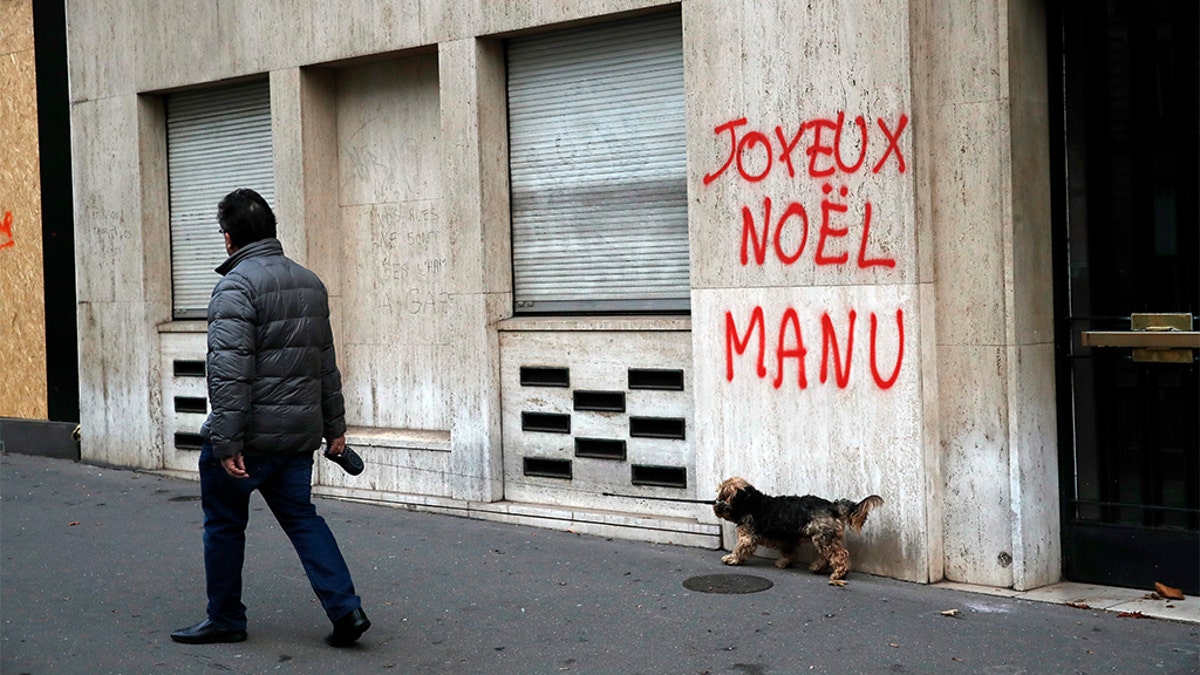 A man walking his dog past a tag reading: Happy Christmas Manu, referring to French President Emmanuel Macron, in Paris, Sunday. (AP Photo/Christophe Ena)