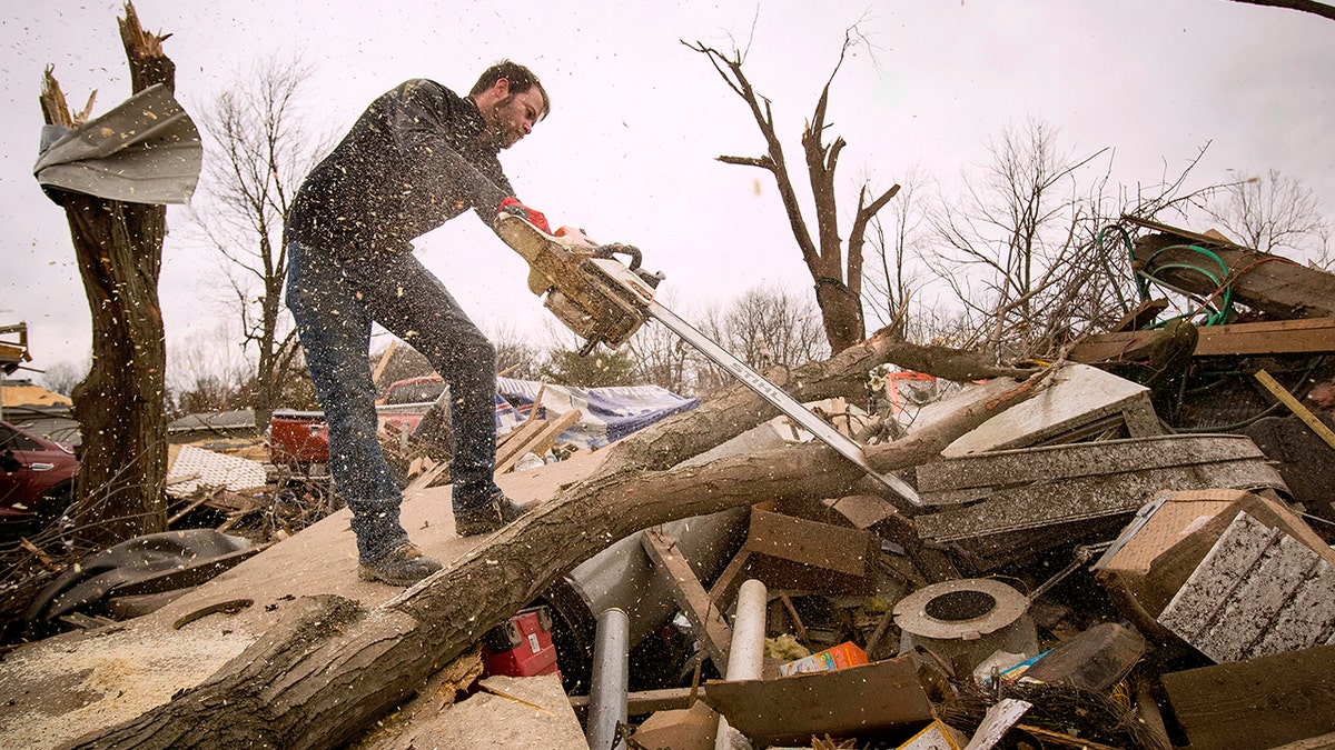 Steven Tirpak using a chainsaw to remove tree branches that fell onto his two-story home in Taylorville, Ill., Sunday. (Ted Schurter/The State Journal-Register via AP)