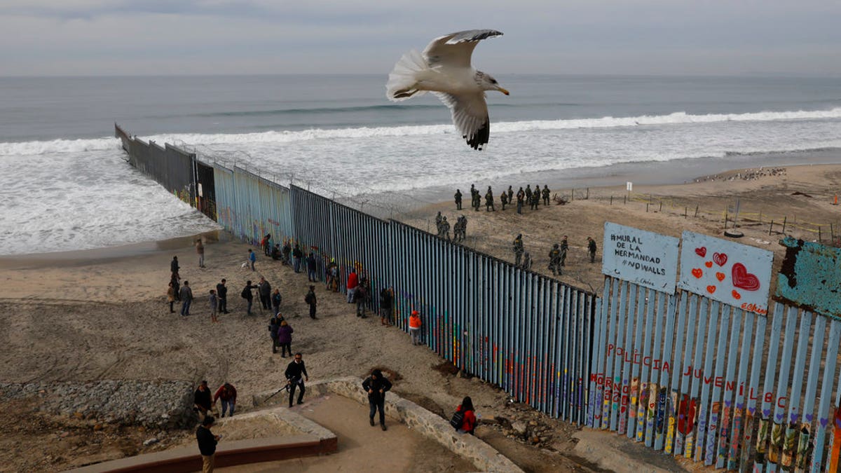 People look on from the Mexican side, left, as U.S. Border Patrol agents on the other side of the U.S. border wall in San Diego prepare for the arrival of hundreds of pro-migration protestors, seen from Tijuana, Mexico, Monday, Dec. 10, 2018. (AP Photo/Rebecca Blackwell)