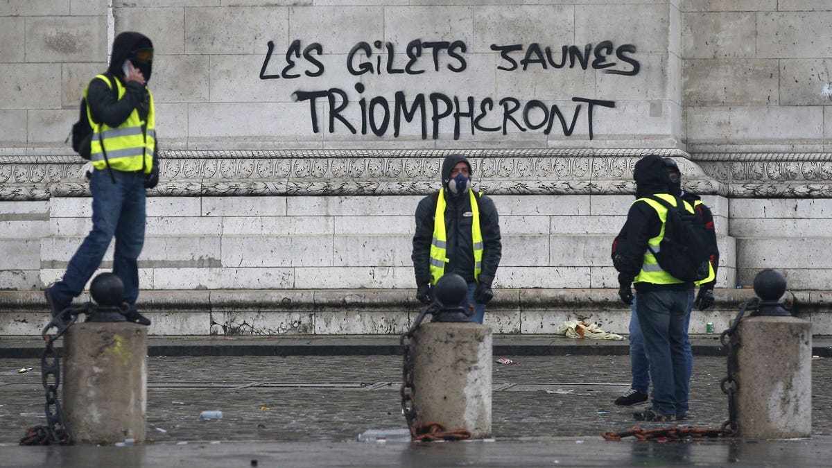 Demonstrators stand by the words "yellow jackets will triumph" written in black letters at the base of the Arc de Triomphe during a demonstration Saturday, Dec.1, 2018 in Paris. 