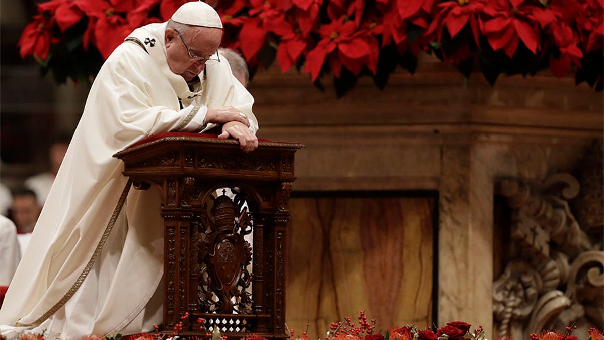 Pope Francis kneels on the altar as he celebrates the Christmas Eve Mass in St. Peter's Basilica at the Vatican.