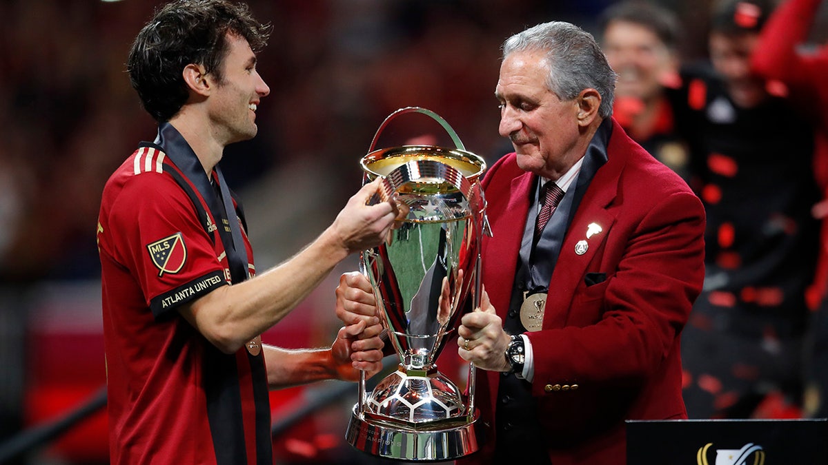 Atlanta United owner Arthur Blank, right, hands the trophy to team captain Michael Parkhurst (3) after the MLS Cup championship soccer game against the Portland Timbers, Saturday, Dec. 8, 2018, in Atlanta. Atlanta United won 2-0. (AP Photo/Todd Kirkland)