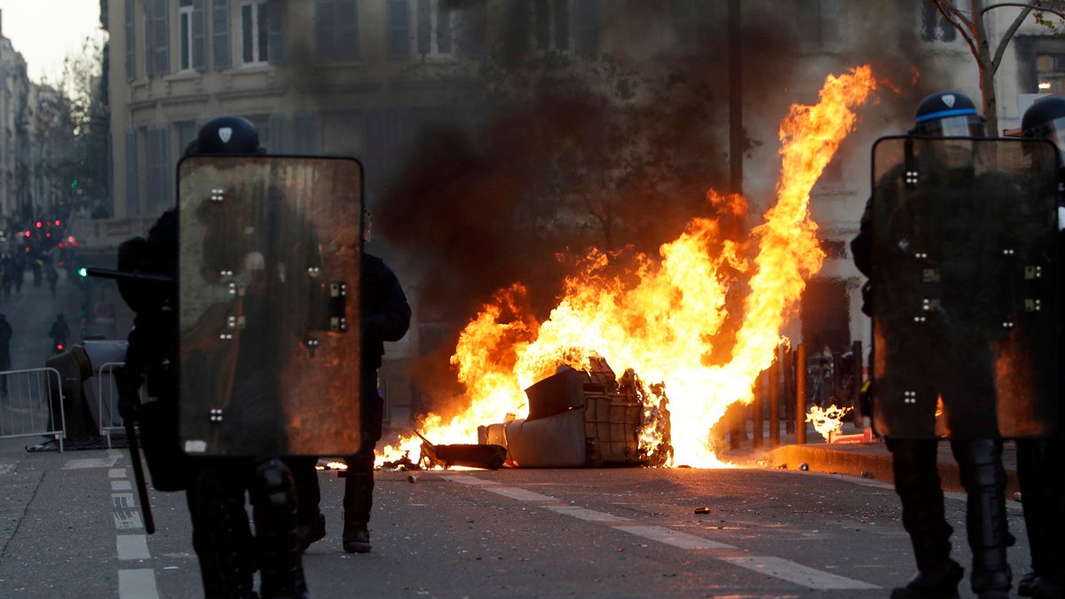 Riot police officers stand in front a burning trash bin during clashes, Saturday, Dec. 8, 2018 in Marseille, southern France.