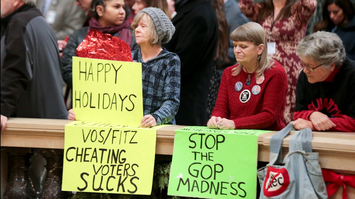 Protesters Peppi Elder, left, and Christine Taylor holding up signs during the state Christmas Tree lighting ceremony in Madison, Wisconsin.