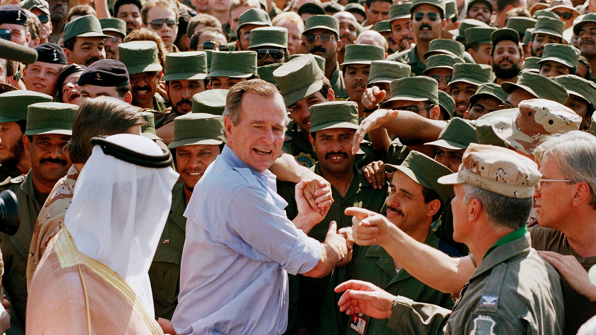 In this Nov. 22, 1990 file photo, President George H.W. Bush is greeted by Saudi troops and others as he arrives in Dhahran, Saudi Arabia, for a Thanksgiving visit. 