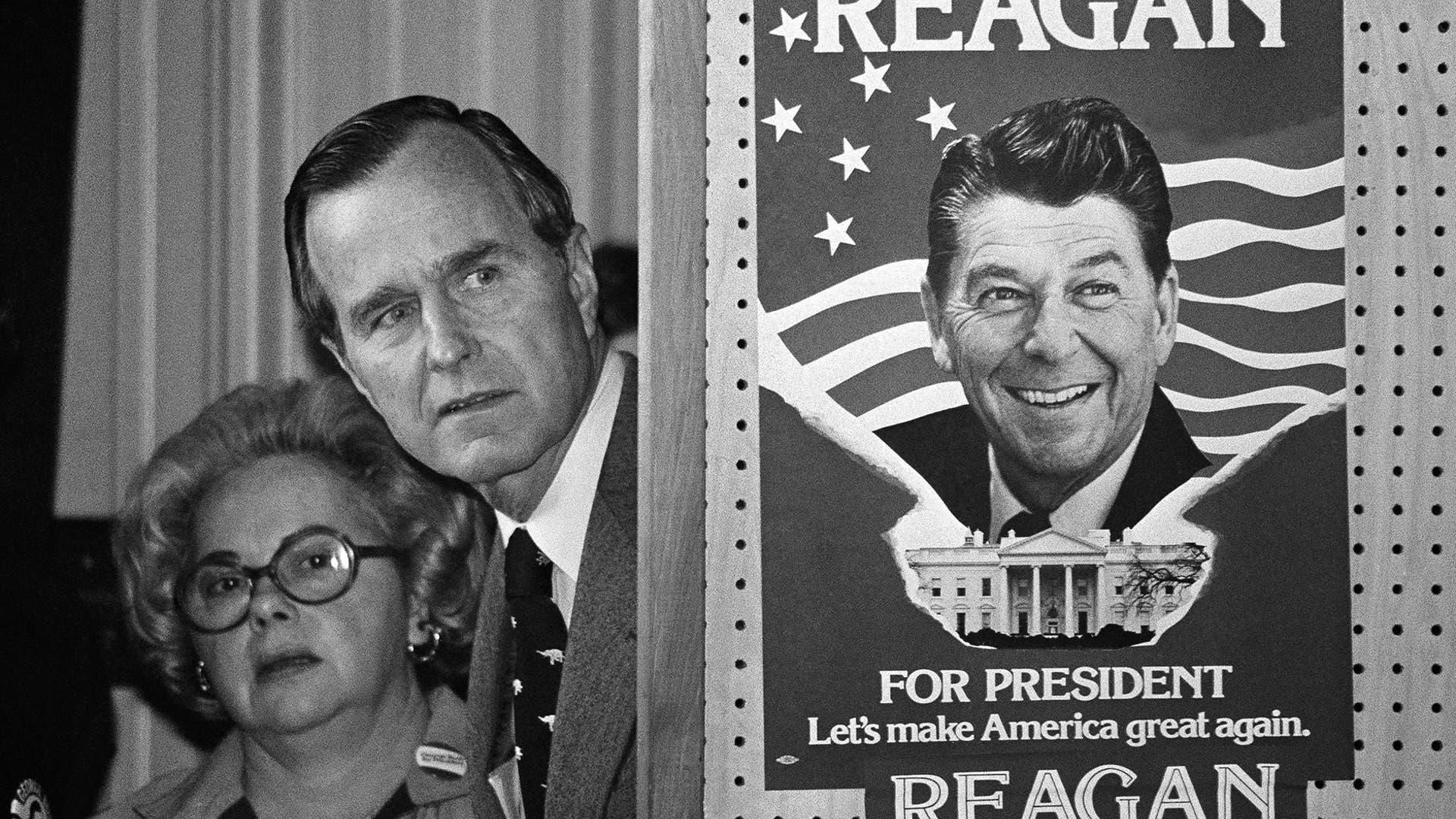 In this March 4, 1980 file photo, George H.W. Bush and an unidentified woman peek around a partition with a poster of Ronald Reagan, one of his opponents for the Republican party presidential nomination, before he speaks in Columbia, S.C.