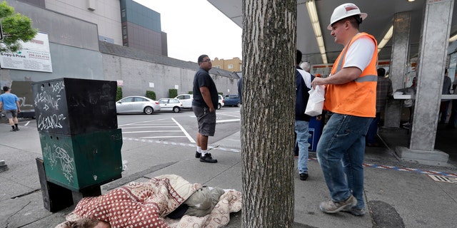 In this May 24, 2018, file photo, a man sleeps on the sidewalk as people behind line-up to buy lunch at a Dick's Drive-In restaurant in Seattle.