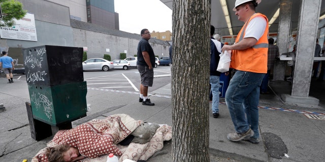 In this May 24, 2018, file photo, a man sleeps on the sidewalk as people behind line-up to buy lunch at a Dick's Drive-In restaurant in Seattle.