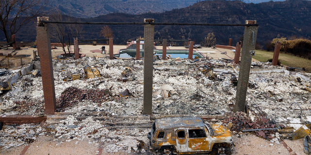 FILE - In this Dec. 3, 2018 file photo, a vehicle rests in front of a home leveled by the Camp Fire in Paradise, Calif. Authorities estimate it will cost at least $3 billion to clear debris of 19,000 homes destroyed by California wildfires last month. State and federal disaster relief officials said Tuesday, Dec. 11, 2018, that private contractors will most likely begin removing debris in January from Butte, Ventura and Los Angeles counties and costs are likely to surpass initial estimates. (AP Photo/Noah Berger, File)