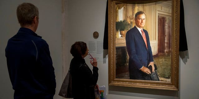 From left, Steve Duensing of Salt Lake City, and Jan Fitzpatrick of Kennebunkport, Maine, look at the official portrait of former President George H.W. Bush as it is draped in black cloth at the National Portrait Gallery in Washington on Monday to mark his passing.