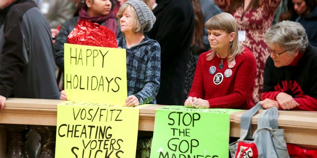 Protesters Peppi Elder, left, and Christine Taylor holds up signs during the state Christmas Tree lighting ceremony in state Capitol Rotunda Tuesday Dec. 4, 2018, in Madison, Wis. The Senate and Assembly are set to send dozens of changes in state law to Gov. Scott Walker's desk. (Steve Apps/Wisconsin State Journal via AP)