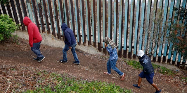 Central American migrants walk along the U.S. border fence looking for places they might be able to cross, in Playas de Tijuana, Mexico, Wednesday, Dec. 5.