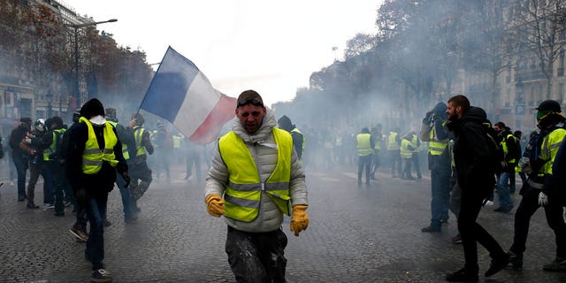 A demonstrator wearing a yellow vest grimaces through tear gas Saturday, Dec. 8, 2018 in Paris. Crowds of yellow-vested protesters angry at President Emmanuel Macron and France's high taxes tried to march Saturday on the presidential palace, surrounded by exceptional numbers of police bracing for outbreaks of violence after the worst rioting in Paris in decades.