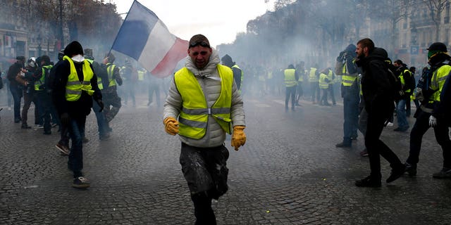 A demonstrator wearing a yellow vest grimaces through tear gas Saturday, Dec. 8, 2018 in Paris. Crowds of yellow-vested protesters angry at President Emmanuel Macron and France's high taxes tried to march Saturday on the presidential palace, surrounded by exceptional numbers of police bracing for outbreaks of violence after the worst rioting in Paris in decades.