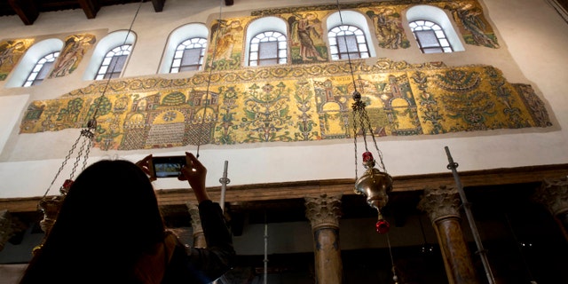 A visitor photographs a renovated part of a fresco inside the Church of the Nativity, built atop the site where Christians believe Jesus Christ was born, in the West Bank City of Bethlehem. (AP Photo/Majdi Mohammed)