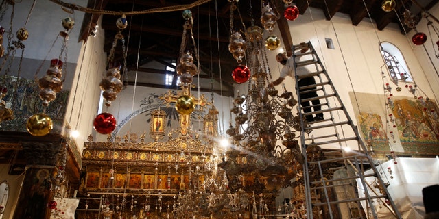 A worker cleans the dust from a chandelier at the Church of the Nativity, built atop the site where Christians believe Jesus Christ was born, in the West Bank City of Bethlehem. (AP Photo/Majdi Mohammed)