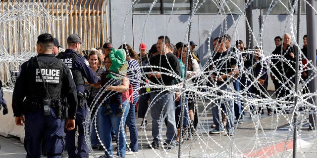 FILE: People line up to cross into the United States from Tijuana, Mexico, seen through barriers topped with concertina wire at the San Ysidro port of entry in San Diego. 