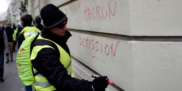 A demonstrator wearing a yellow vest writes a slogan 'Macron resign' on a wall during a protest Saturday, Dec. 15, 2018 in Paris. (AP Photo/Kamil Zihnioglu)