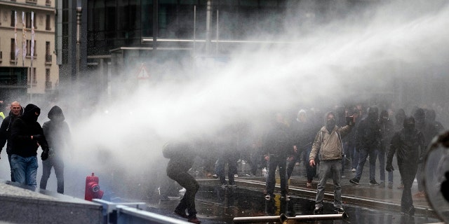Protestors are held back by a police water cannon during an anti-migrant demonstration outside of EU headquarters in Brussels, Sunday, Dec. 16, 2018. (AP Photo)