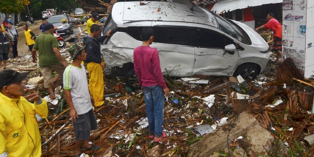 In this Sunday, Dec. 23, 2018, photo, people inspect the wreckage of a car swept away by a tsunami in Carita, Indonesia. The tsunami that hit the coasts of Indonesian islands along the Sunda Strait was not big but it was destructive. The waves smashed onto beaches in the darkness Saturday night without warning, ripping houses and hotels from their foundations in seconds and sweeping terrified concertgoers into the sea. (AP Photo)