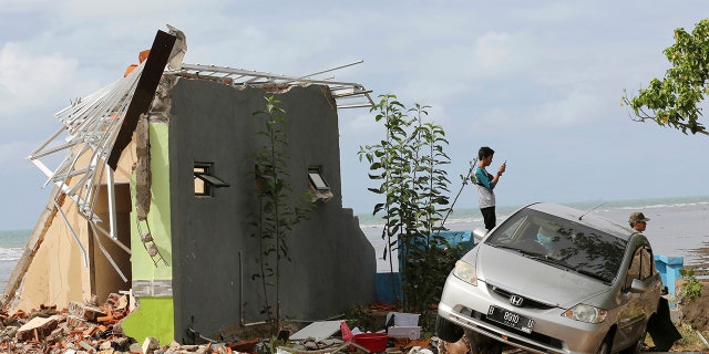 A man takes a photo with his mobile phone at a cottage damaged by a tsunami in Carita beach, Indonesia, Monday, Dec. 24, 2018. Doctors worked to save injured victims while hundreds of military and volunteers scoured debris-strewn beaches in search of survivors Monday after a deadly tsunami gushed ashore without warning on Indonesian islands on a busy holiday weekend. (AP Photo/Tatan Syuflana)