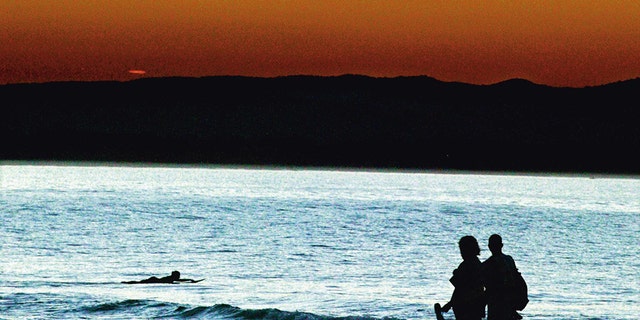 A couple stroll along a Byron Bay beach at sunset.