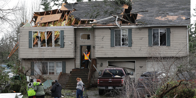 People stand in front of a damaged home, Wednesday, Dec. 19, 2018, in Port Orchard, Wash., the day after a tornado caused heavy damage in the area Tuesday. (AP Photo/Ted S. Warren)