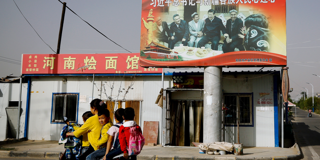 An Uighur woman uses an electric-powered scooter to fetch school children as they ride past a picture showing China's President Xi Jinping joining hands with a group of Uighur elders at the Unity New Village in Hotan, in western China's Xinjiang region. (AP Photo/Andy Wong, File)