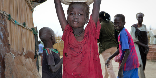 In this photo taken Sunday, December 9, 2018, a young girl carries water on her head in Koythiey displaced camp on the outskirts of Bentiu town in South Sudan. Six months ago, planning ahead in the civil war skin South Sudan was apparently impossible, but now, after the warring parties signed a new peace agreement in September that government promises will hold, some have begun to rebuild their lives.